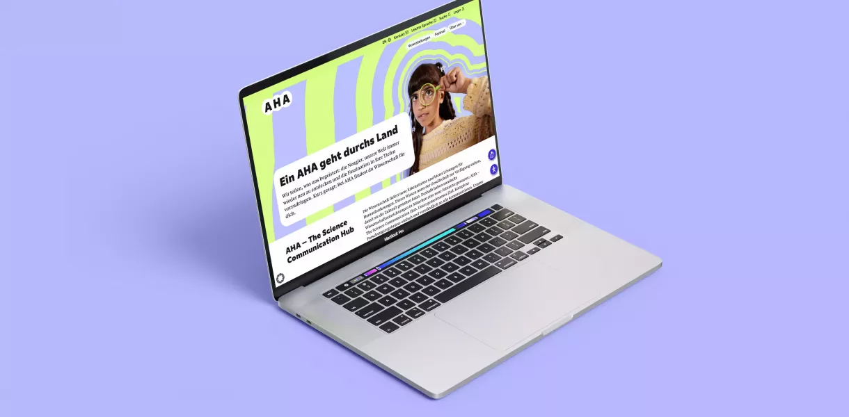 Open laptop on purple background, with the AHA website displaying a green and purple pattern on the screen, person with magnifying glass and text \