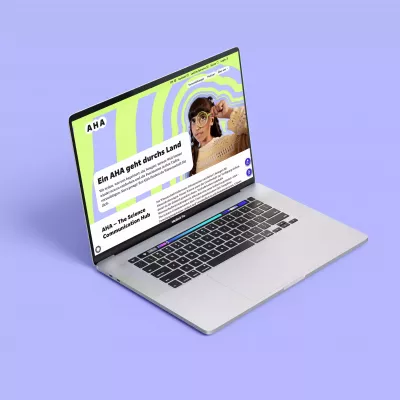 Geöffneter Laptop auf lilafarbenem Hintergrund, auf dem Bildschirm die AHA-Webseite mit grün-lila Muster, Person mit Lupe und Text \
