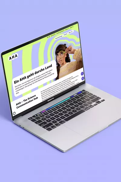 Open laptop on purple background, with the AHA website displaying a green and purple pattern on the screen, person with magnifying glass and text \
