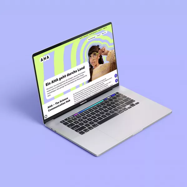 Open laptop on purple background, with the AHA website displaying a green and purple pattern on the screen, person with magnifying glass and text \