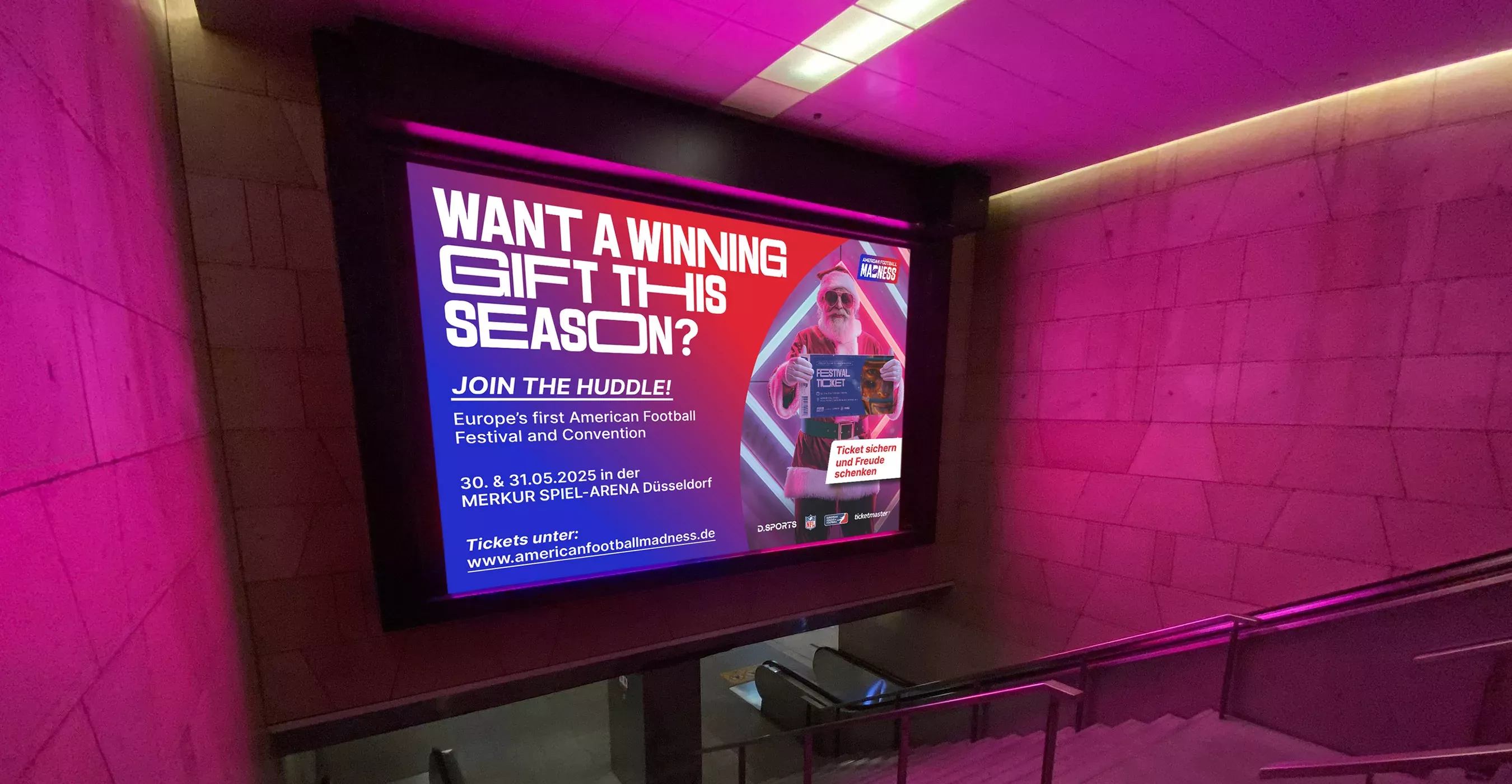 Digitale Werbetafel in pink beleuchtetem U-Bahntunnel zeigt Weihnachtsmann mit Sonnenbrille und Ticket, Text \