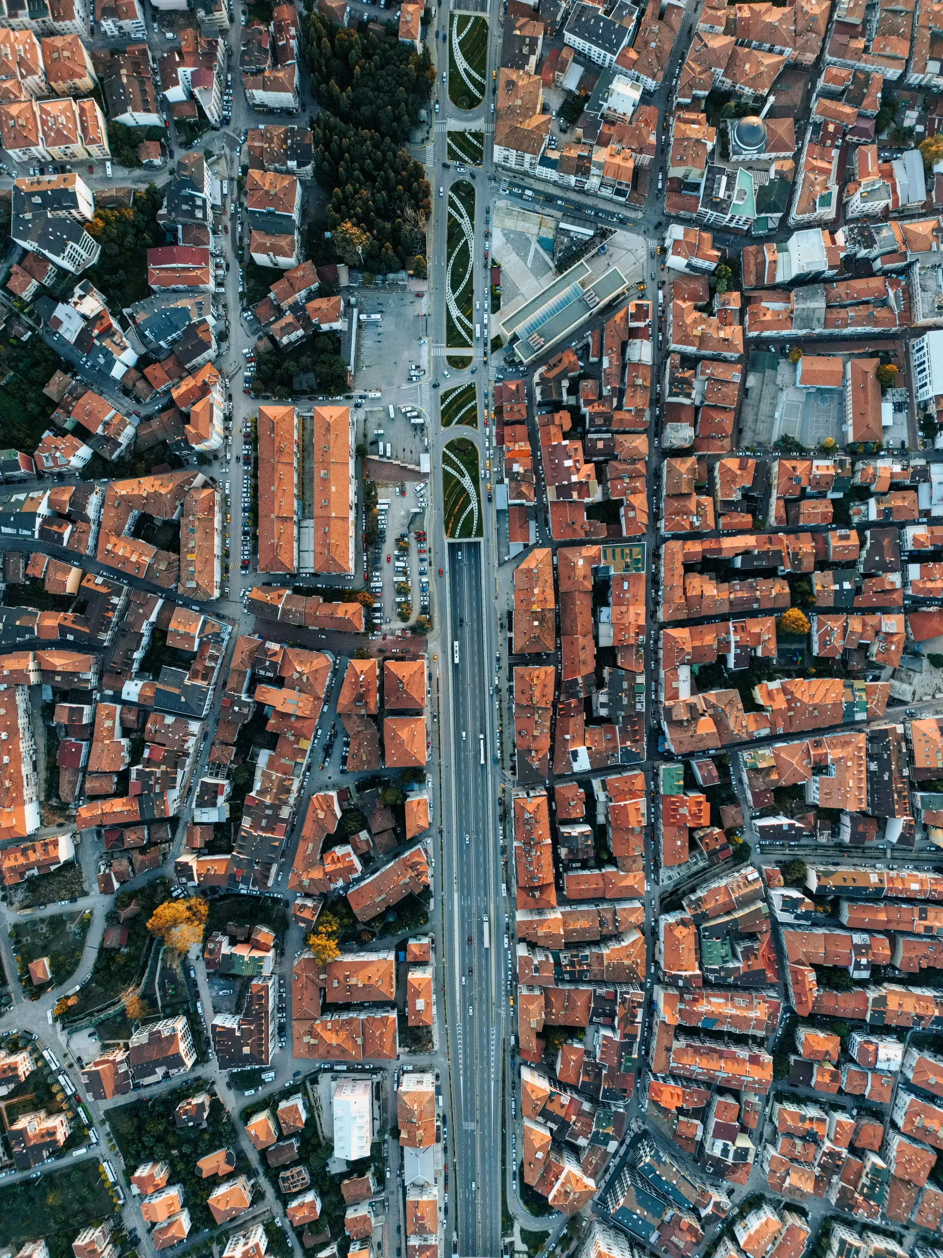 Luftaufnahme einer dicht bebauten Stadt mit roten Dächern, durchzogen von einer breiten mehrspurigen Straße