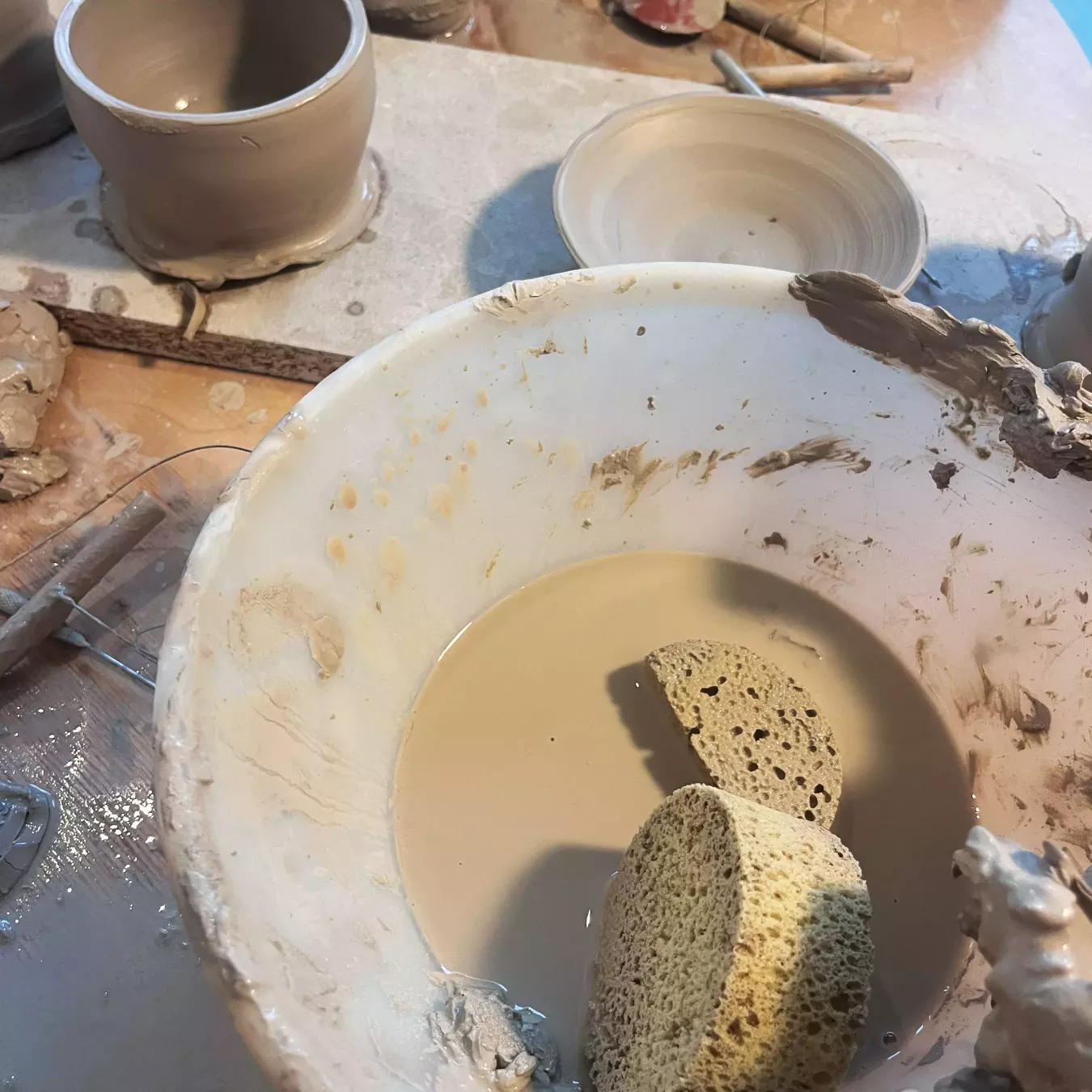 Schüssel mit Tonwasser und Schwamm, daneben Werkzeuge und frisch geformte Töpferstücke