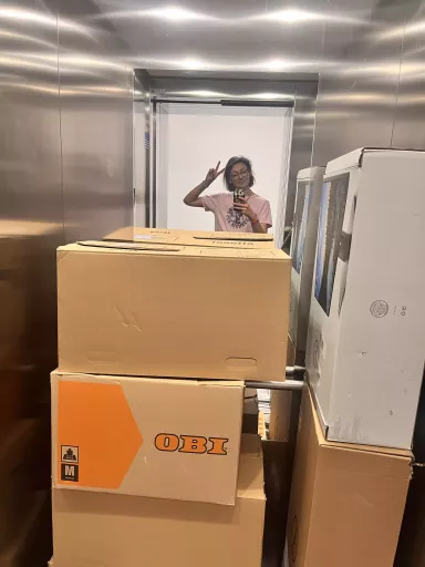Spiegel-Selfie von Lea im Aufzug vom dimedis Büro, umgeben von gestapelten Umzugskartons mit \