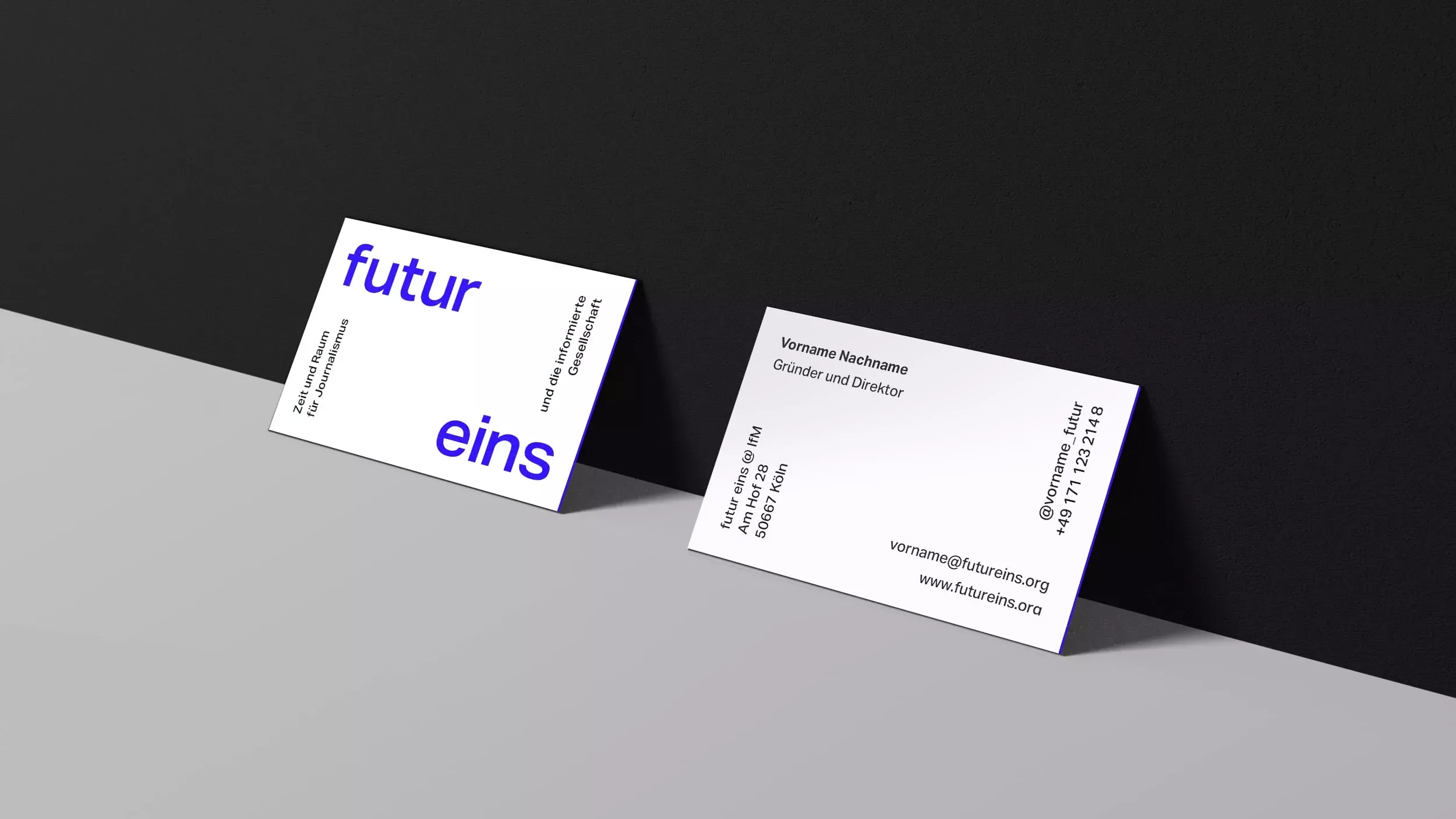 Two business cards on a gray background leaning against a black wall with the \