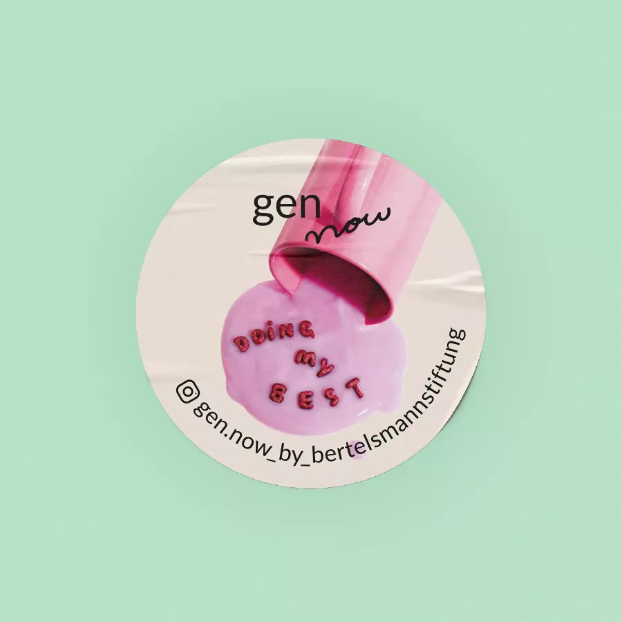 Runder Sticker von gen now mit pinkem Becher, aus dem rosafarbene Flüssigkeit läuft, in der die Buchstaben „DOING MY BEST“ schwimmen, auf mintgrünem Hintergrund