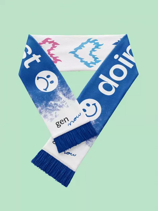 Blauer und weißer Schal mit gen now Logo, Smiley-Motiven und Flammenherz-Illustrationen, auf mintgrünem Hintergrund