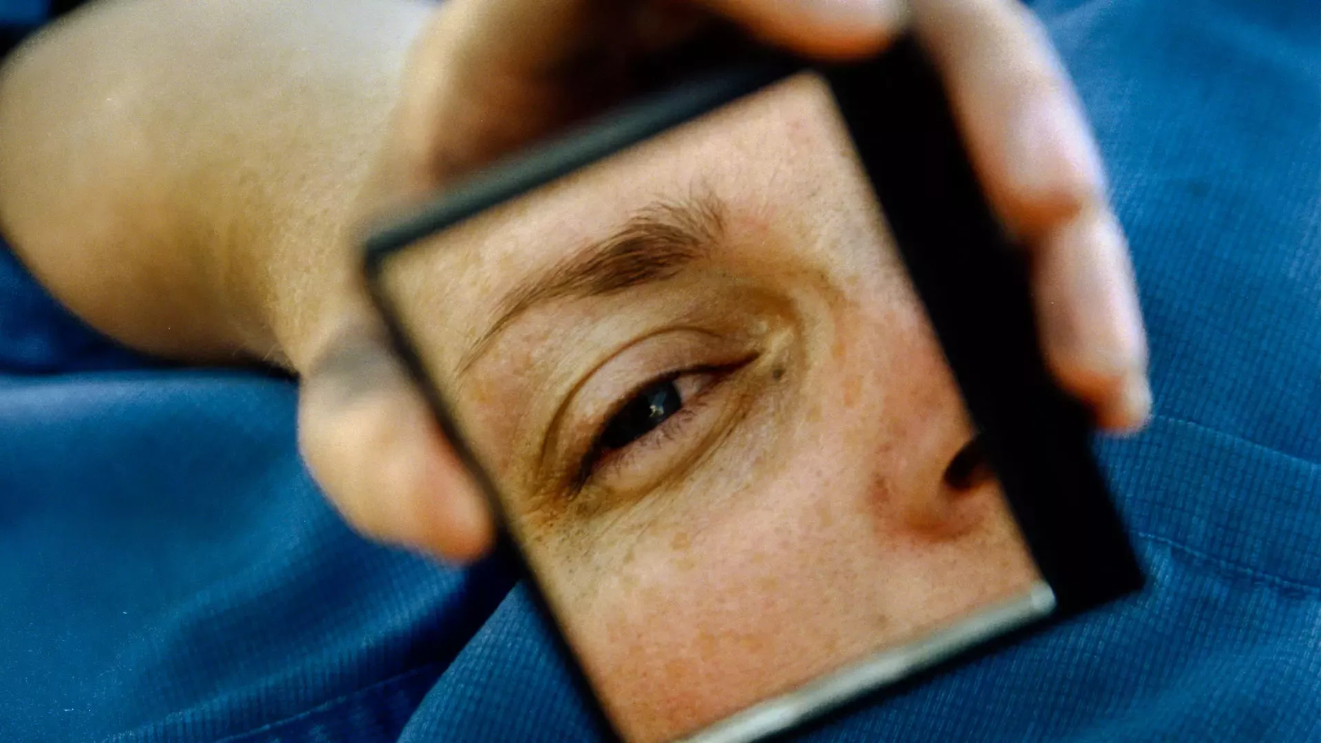 Close-up of a face with one eye reflected in a small mirror held by the person's hand