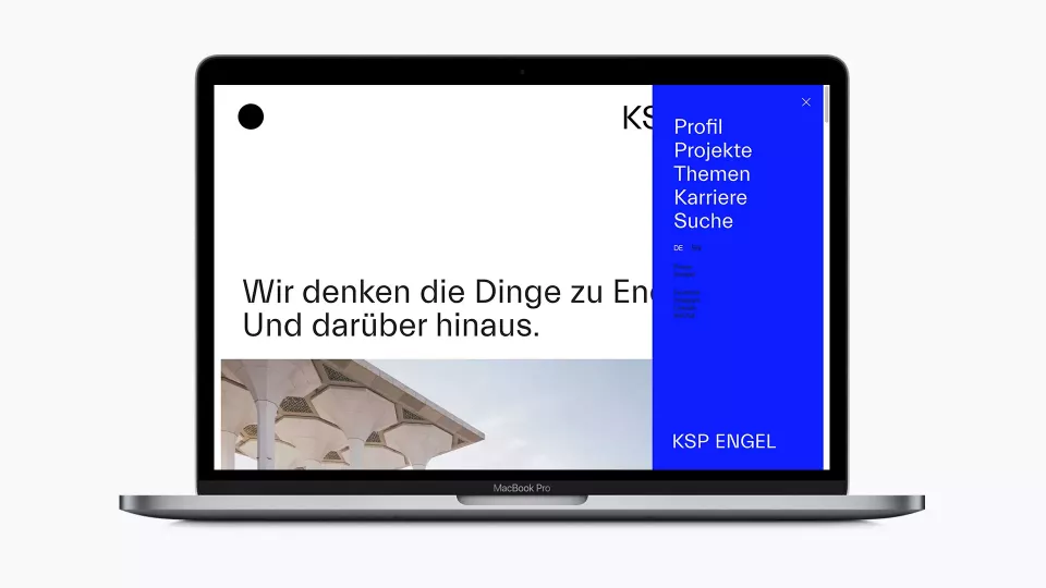 Open laptop showing the homepage of the KSP Engel Architekten website with the headline „Wir denken die Dinge zu Ende Und darüber hinaus“ (We think things through to the end and beyond.). The blue navigation bar is open on the right