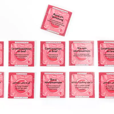 Several information brochures designed to look like condom packaging with a red background, labeled in various languages with information on contraception in Switzerland