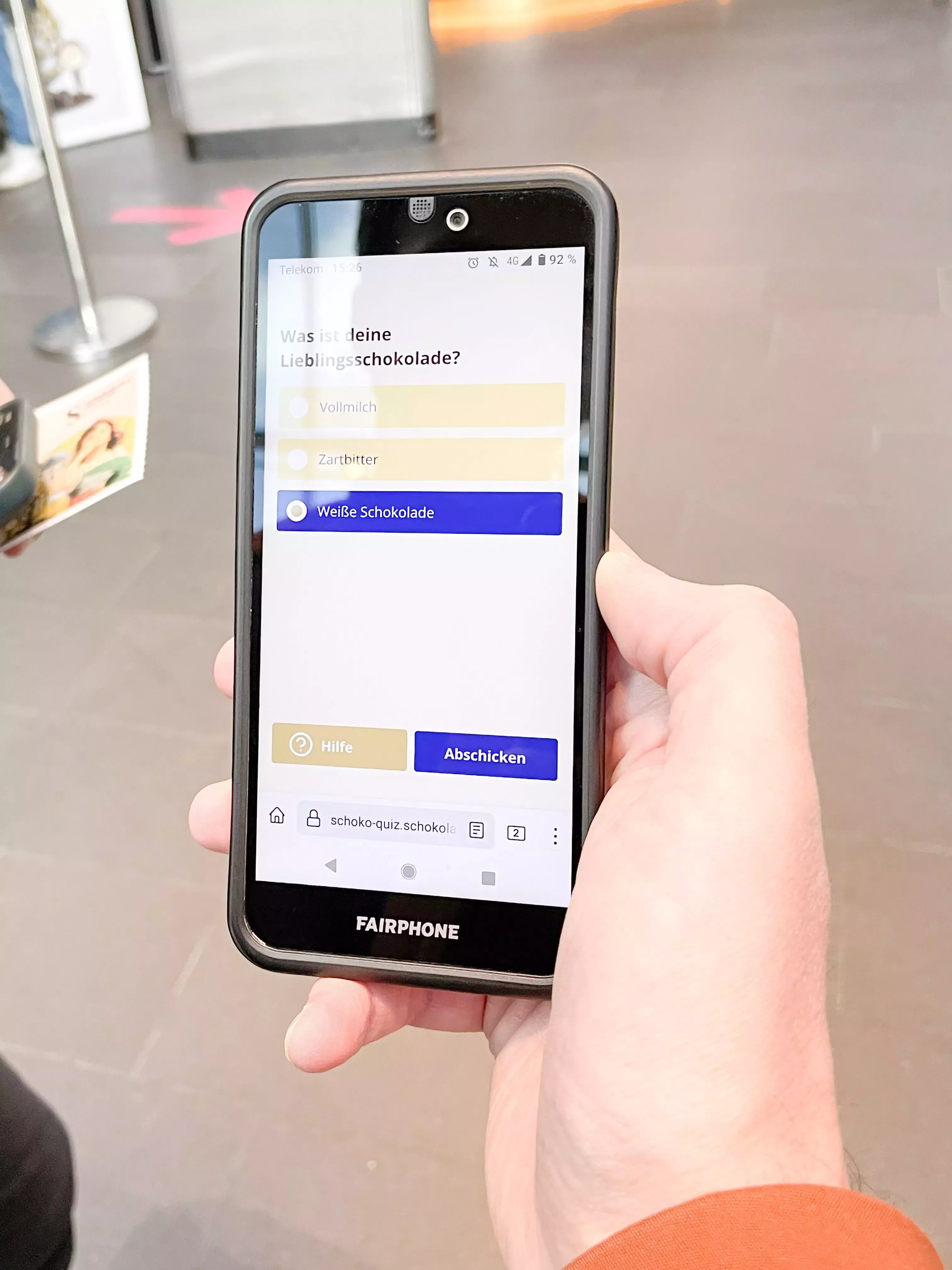 Hand hält ein Smartphone mit geöffneter Quizfrage „Was ist deine Lieblingsschokolade?“ – ausgewählt ist „Weiße Schokolade“