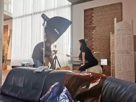 Videodreh in hellem Loft, Person sitzt vor Kamera mit Ringlicht, zwei Personen bedienen die Kamera, daneben große Softbox, im Hintergrund rote Ziegelwand und Paravent