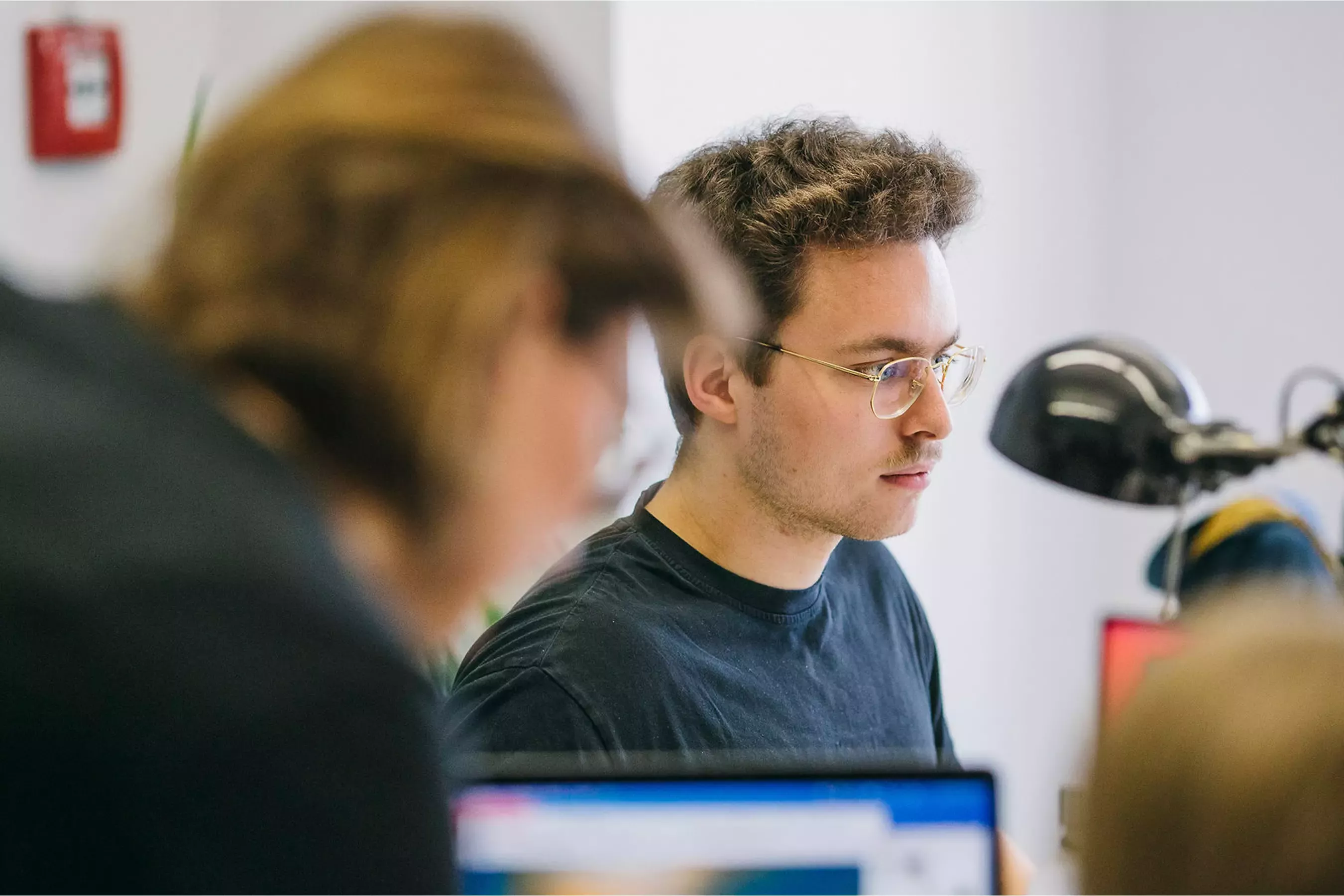 Nico sits concentrating at his workstation in front of a monitor, with Lea blurred in the foreground