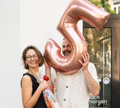 Lea und Steffen vor dem Büro mit großer Ballonzahl \