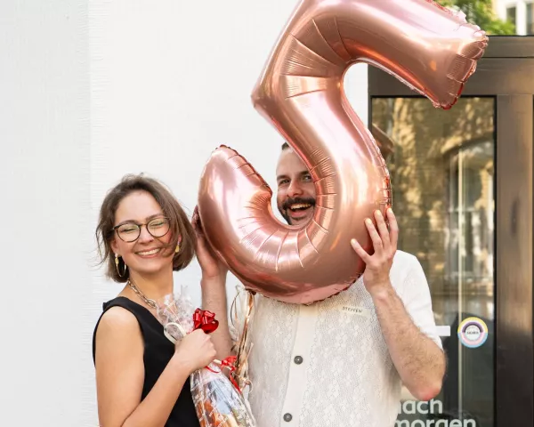 Lea und Steffen vor dem Büro mit großer Ballonzahl \