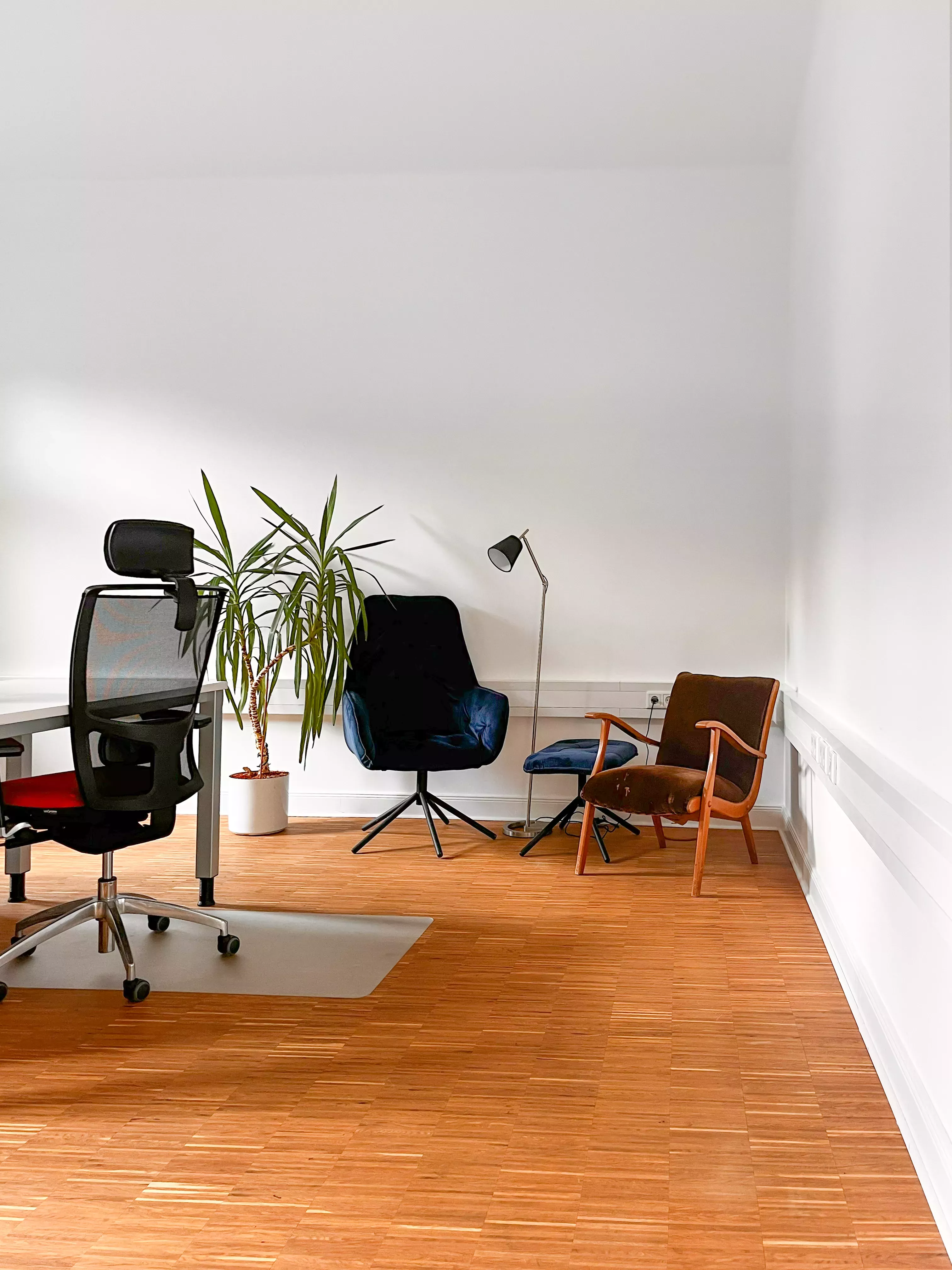 Foto vom Büro, ein Schreibtisch im Anschnitt, zwei Sessel und eine Lampe stehen in der Ecke. Die Stimmung ist hell und der Boden ist aus Echtholz.
